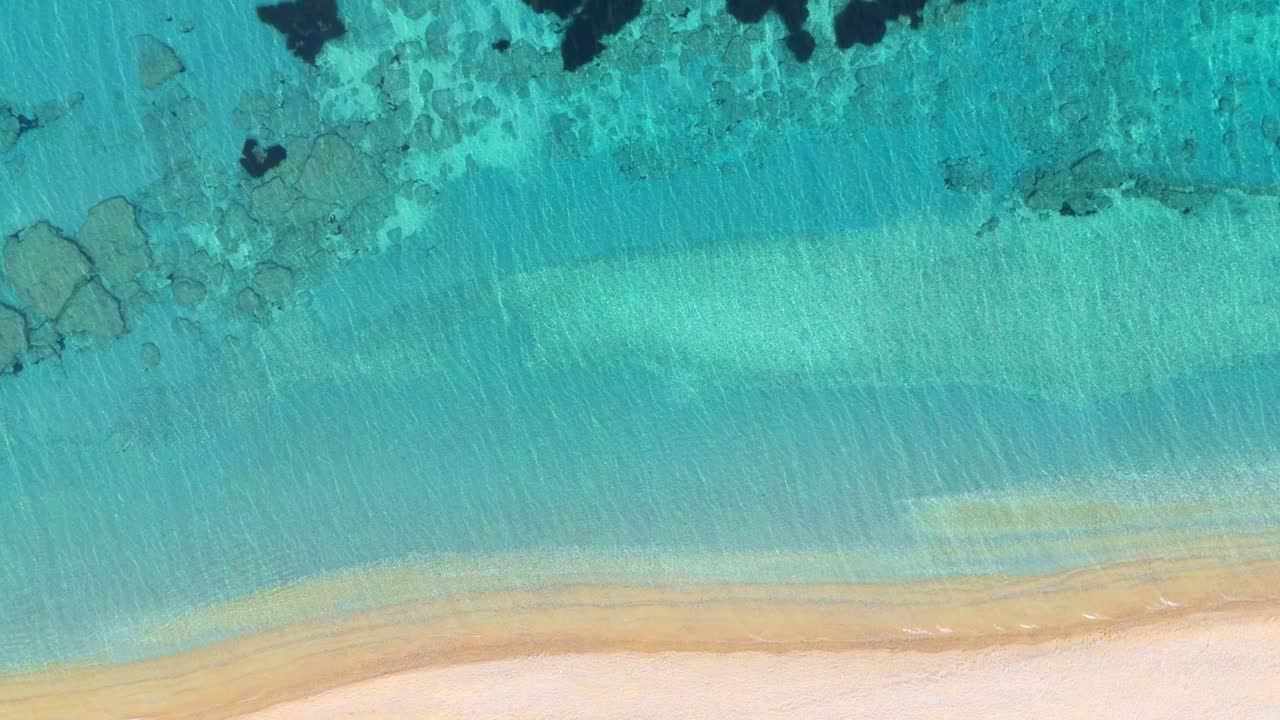 Drone perspective over Myrtos Beach, Kefalonia, Greece, highlighting vivid blue sea, white sandy beaches, and rugged cliffs bathed in warm Mediterranean sunlight.