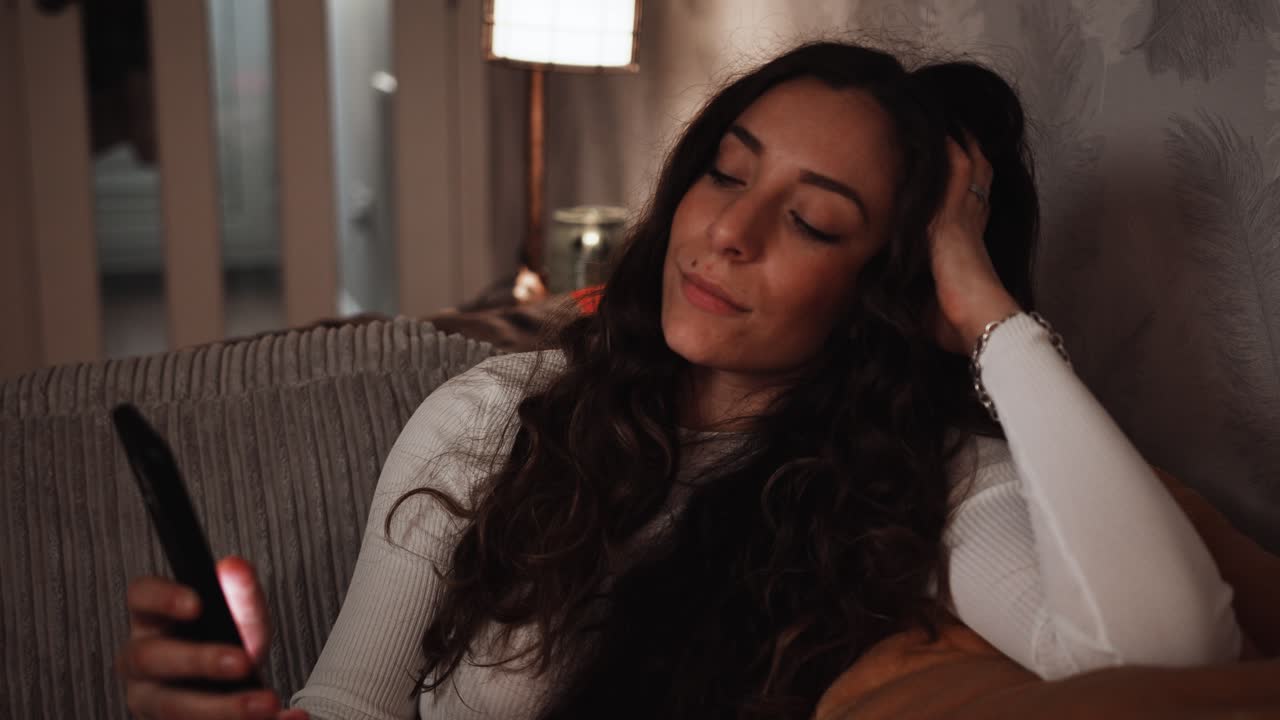 joven italiana se relaja en el sofá mientras se desplaza sin rumbo por su teléfono