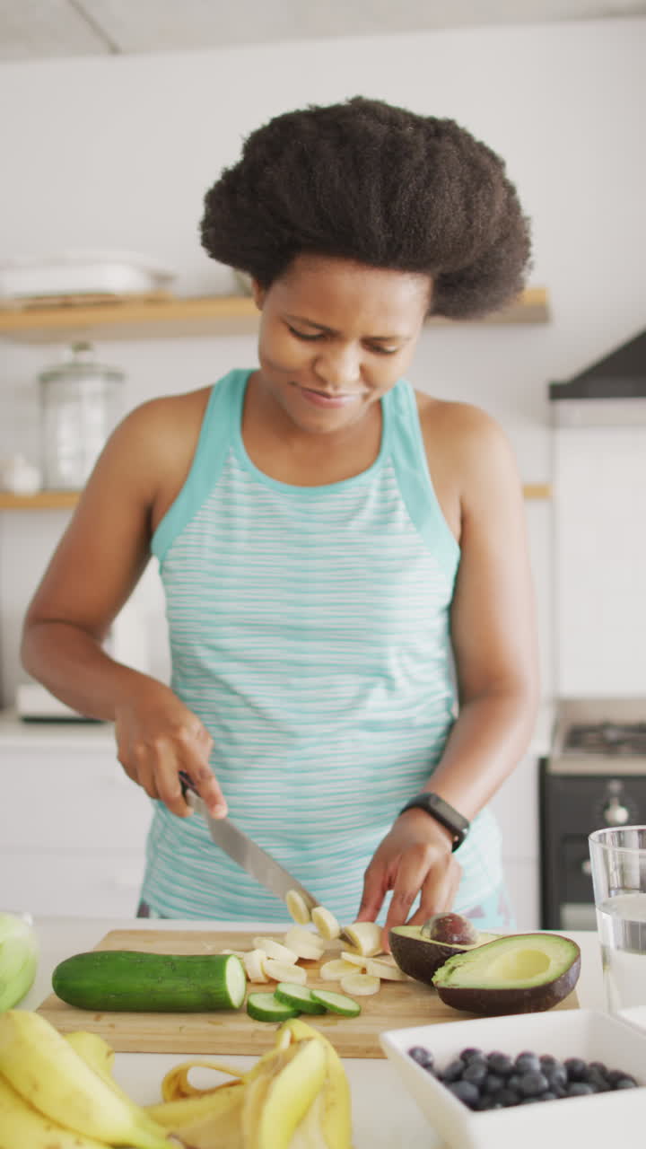 Video verticale di una donna afroamericana sorridente che taglia verdure in cucina.