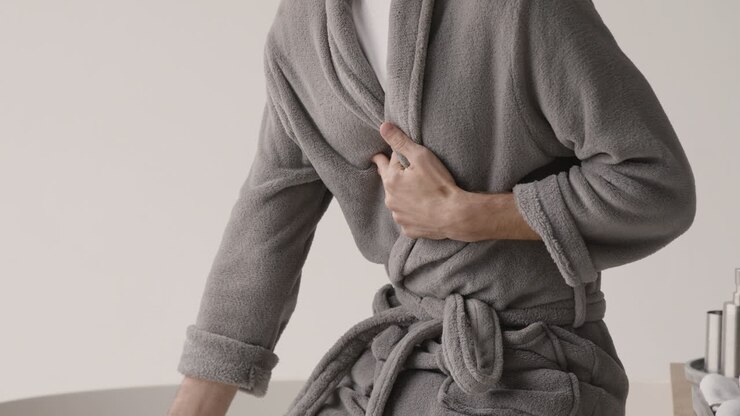 Uomo sofferente in abiti e vestaglia con dolore al petto che si tocca la zona del cuore al mattino a casa