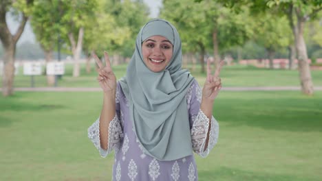 happy muslim woman showing victory sign in park