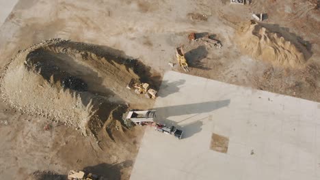 Vista-Aérea-De-Un-Camión-Volquete-Que-Descarga-Su-Carga-De-Materiales-En-Un-Sitio-De-Construcción-En-Un-Día-Nublado-De-Invierno-Al-Sur-De-Boston