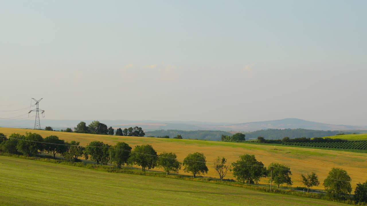 Hilly landscape during a sunny day of a field of meadows and power poles