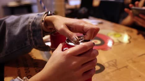 hands opening a cola can on a table