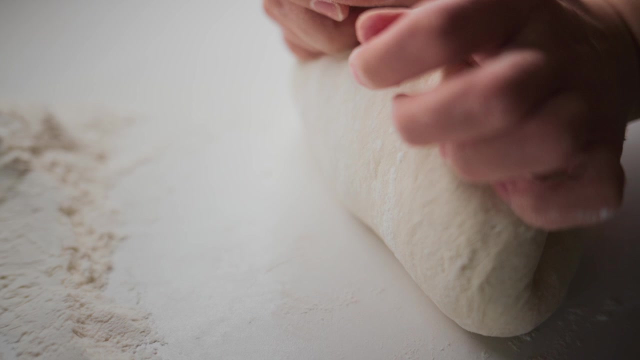 Close-up hands knead dough on floured surface. Gentle motion shows care and focus. Ideal for cooking, baking, or food-related content. Warm tone highlights homemade comfort and tradition