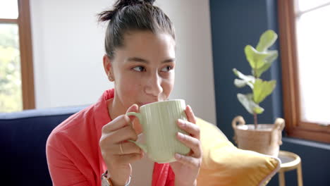 retrato de una adolescente biracial feliz sentada en casa bebiendo té, espacio de copia, cámara lenta