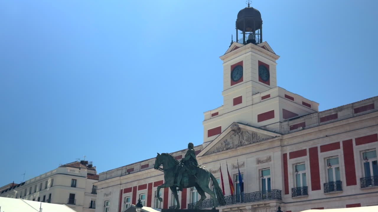 Smooth lateral pan of the iconic Puerta del Sol clock tower and equestrian statue in Madrid, Spain. Historic landmark captured on a clear, sunny day