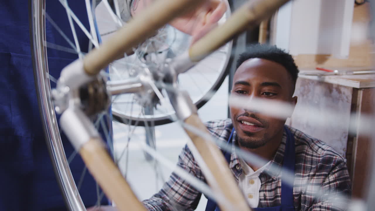 Male Trainee In Workshop Checking Wheel Of Hand Built Bicycle Frame