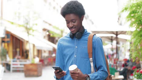 african american man holding coffee to go and using smartphone in the street