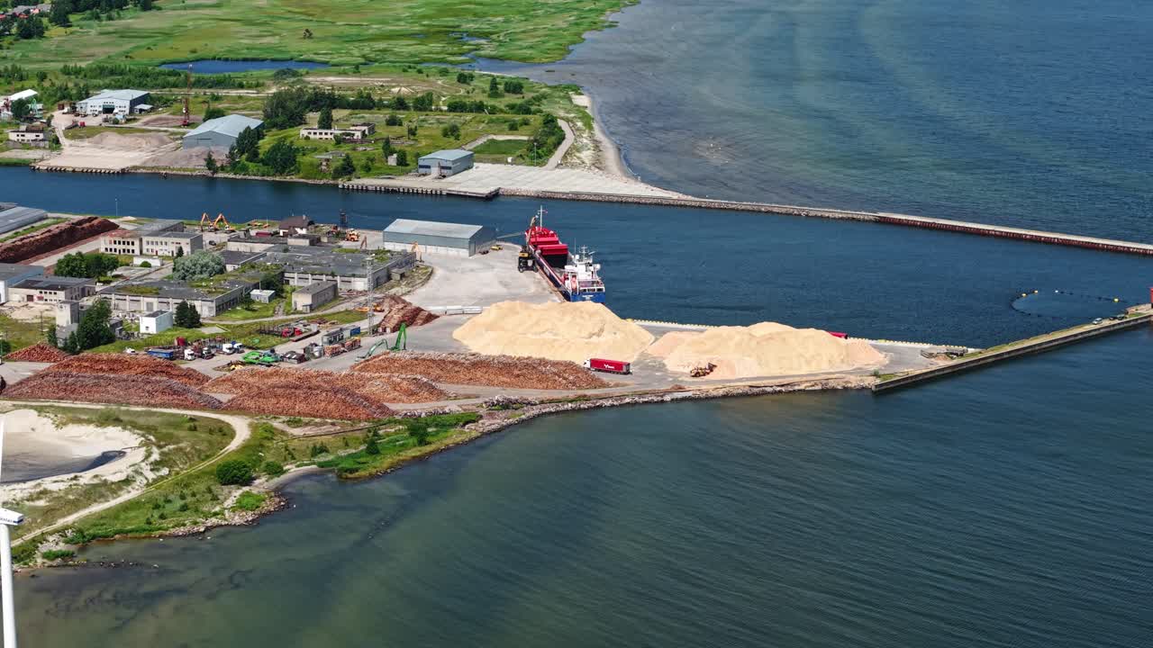 Aerial of cargo ship at port with of land, shoreline, and sea under blue sky