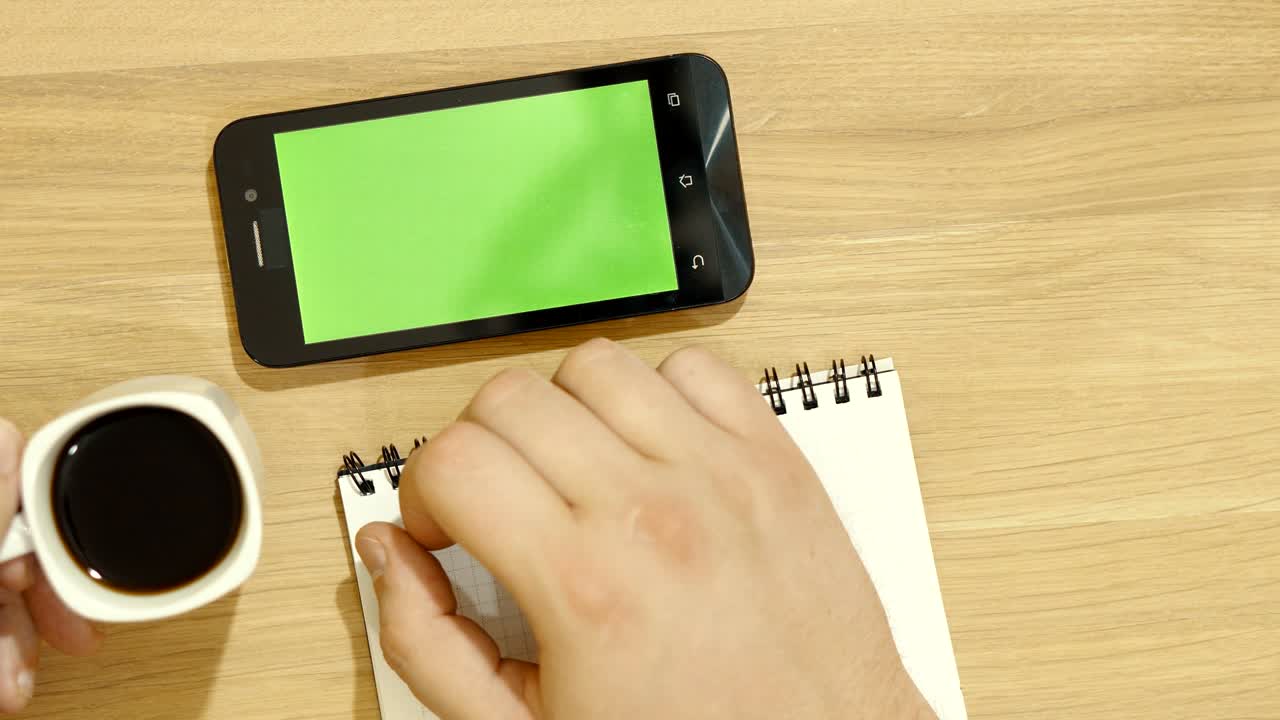 The specialist is sitting at the desk. The hand works with the tablet. A cup of coffee on the table. Green screen.