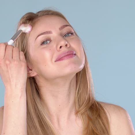 beautiful blond woman applying makeup powder on her face using brush