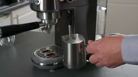 un hombre espumando leche usando la varita de vapor de una elegante máquina de espresso, sosteniendo una jarra de acero inoxidable