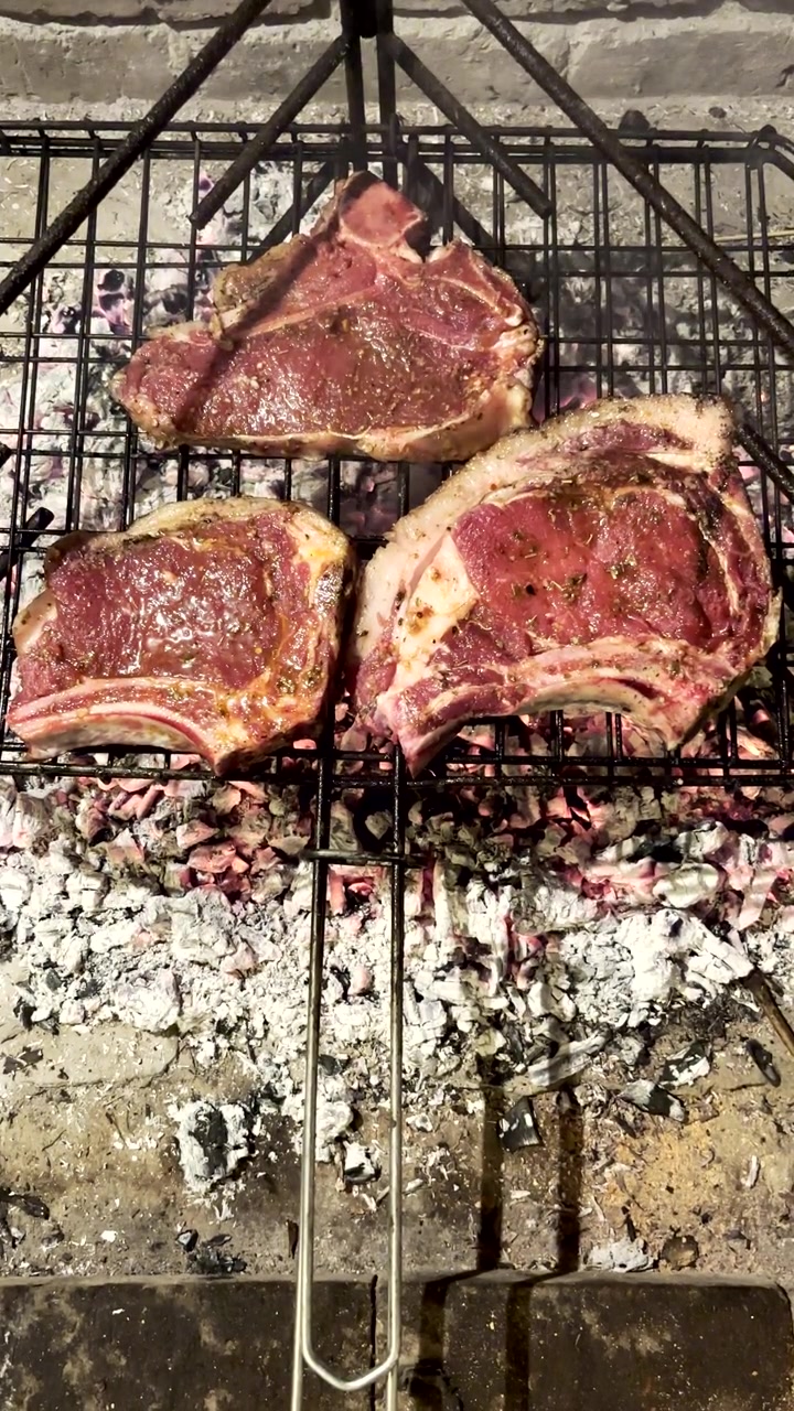 Steak T-bone mentah yang dibumbui di atas panggangan kawat dipanggang di atas bara panas. Tampilan atas vertikal