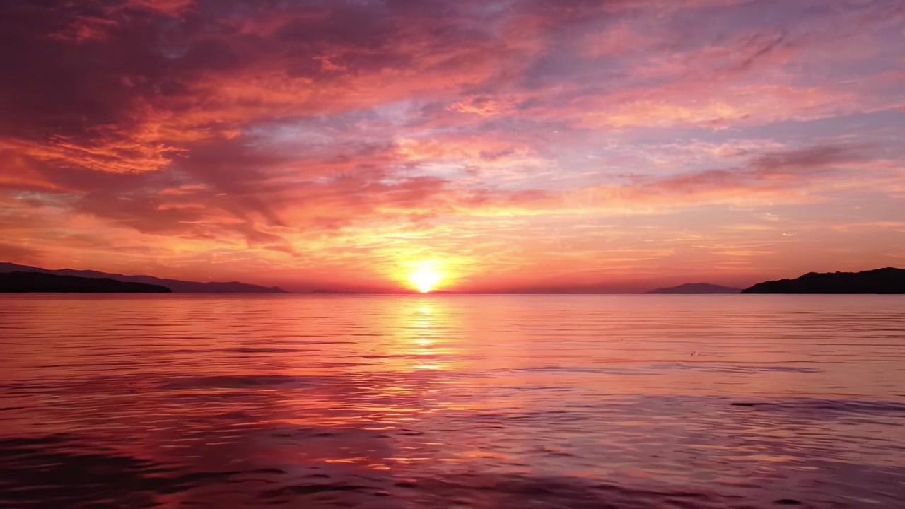 Un tramonto mozzafiato su acque calme, con splendide sfumature di tonalità arancioni, rosa e viola che si riflettono sulla serena superficie dell'oceano.
