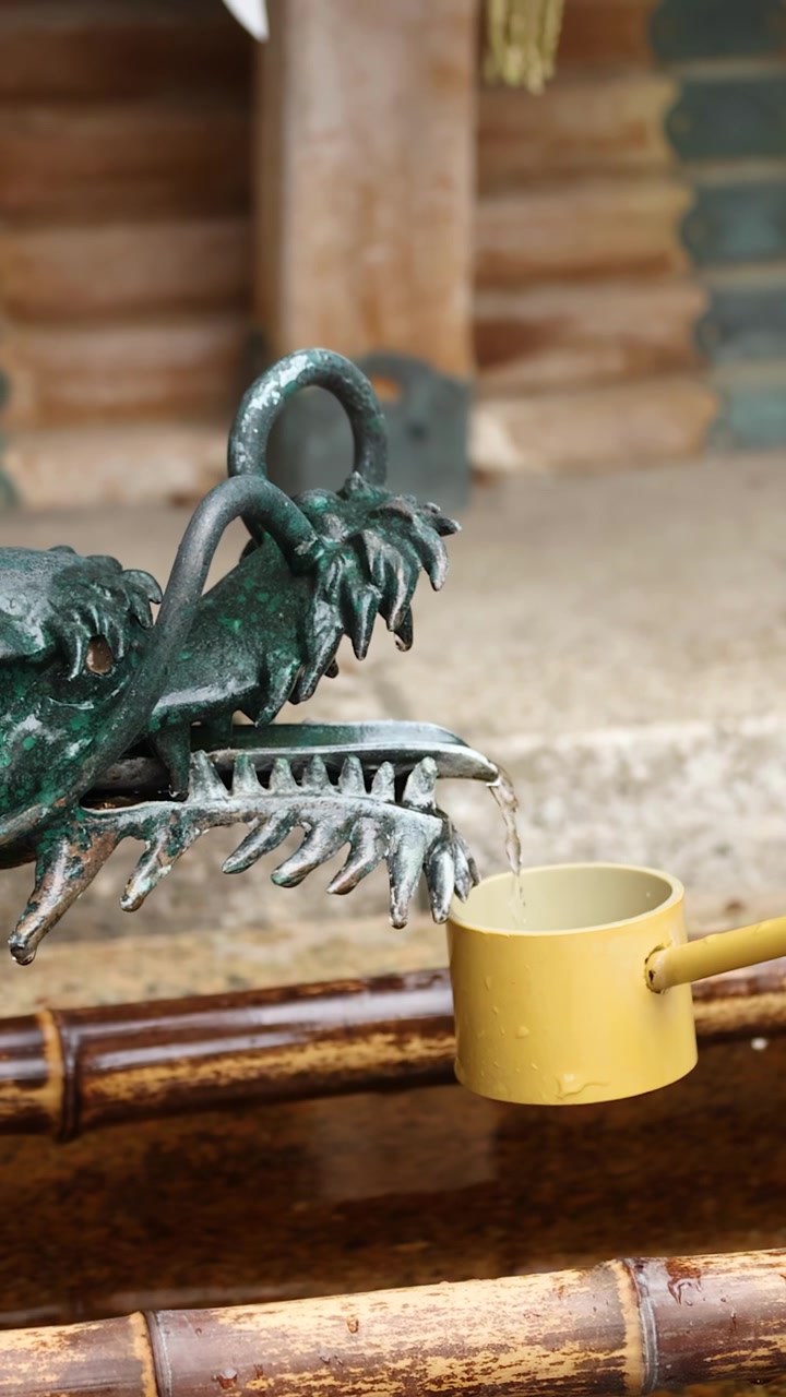 Close-up of water flowing from a bronze dragon statue into a bamboo ladle in Tokyo.