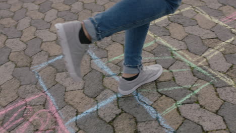 close up teenage girl playing hopscotch game jumping on colorful squares in school playground having fun outdoors