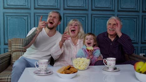 Multigenerational-happy-family-laughing,-watching-cartoons-television-movies,-eating-popcorn-at-home