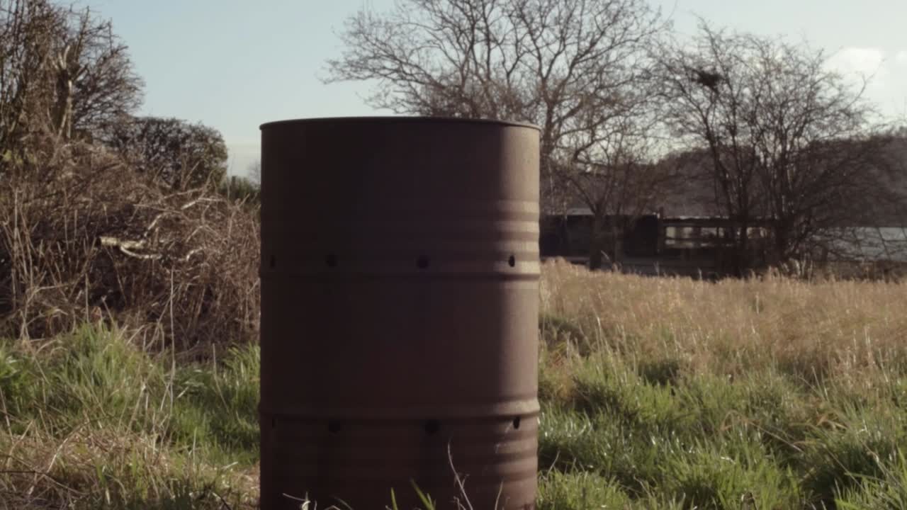 Rusty oil drum abandoned in a field wide panning shot