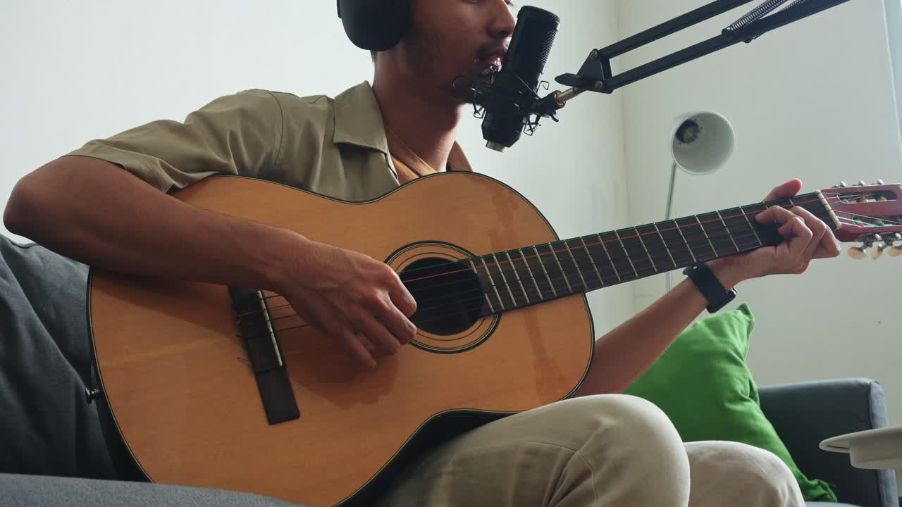 Close-up of musician's hands on guitar while records song in living room