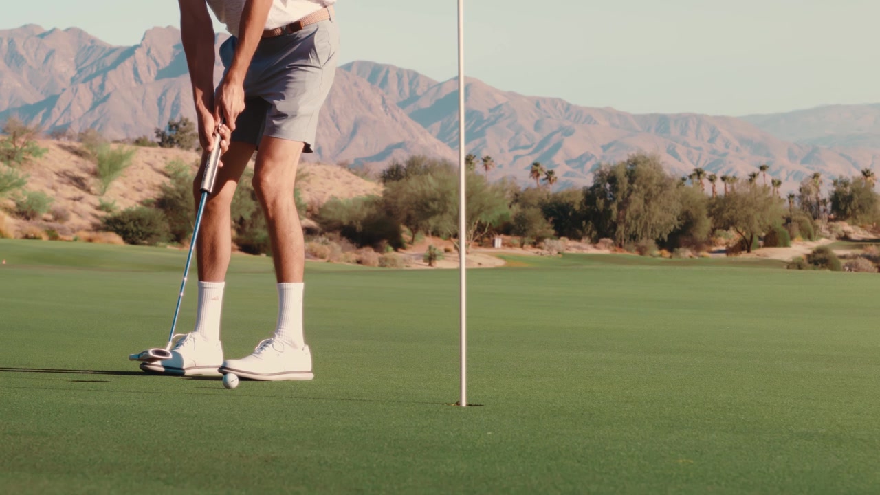 Un golfista imbuca un putt mentre la palla rotola verso l'asta della bandiera su un green desertico al crepuscolo, filmato in ultra slow motion, ottimo per il marketing del golf, promozioni sportive e branding di resort.