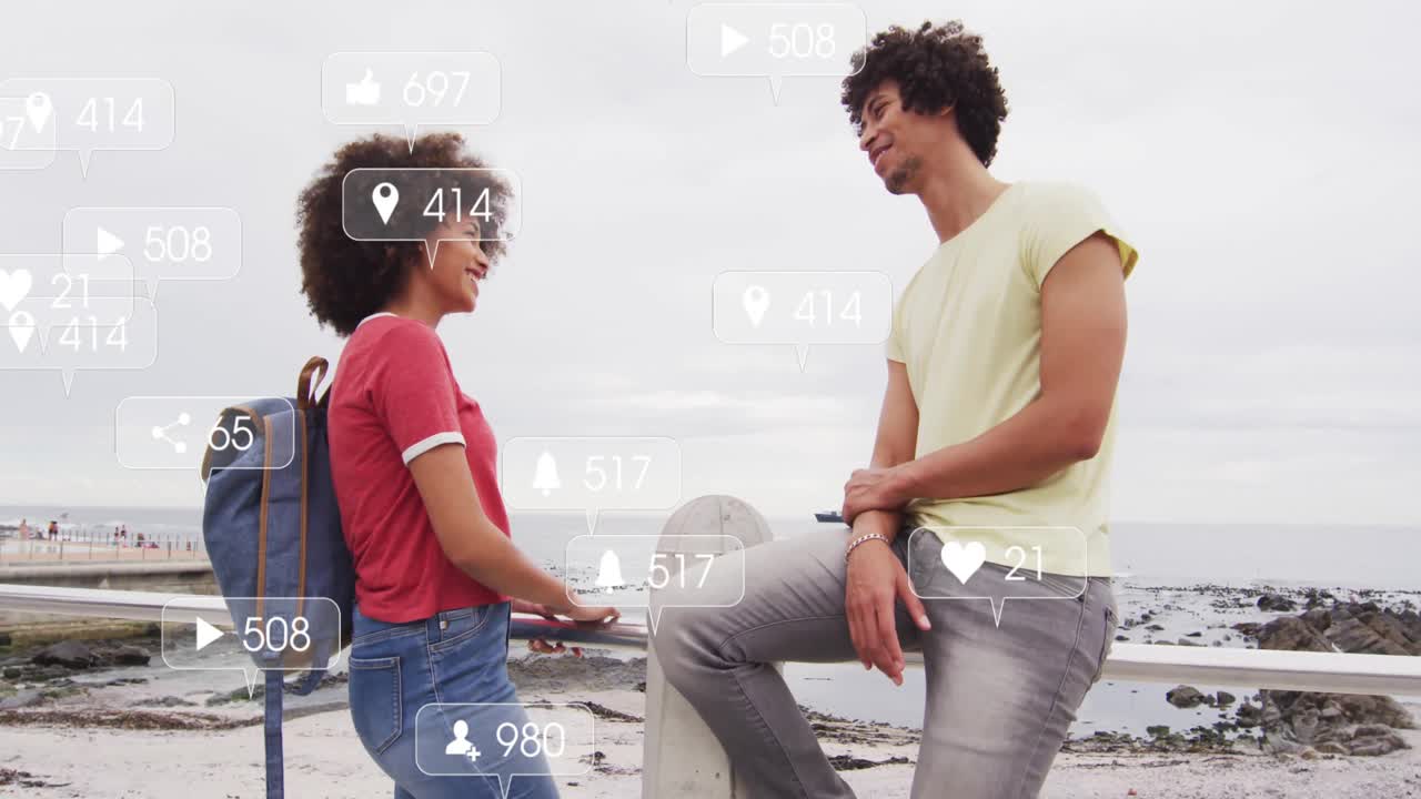 Interacting by sea, two people with animation of social media icons overlaying