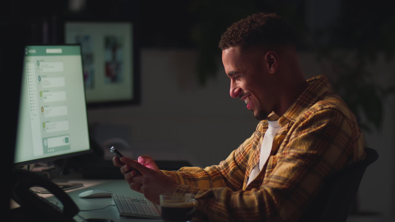 Businessman Working Late In Office With Face Illuminated By Computer Screen Using Mobile Phone