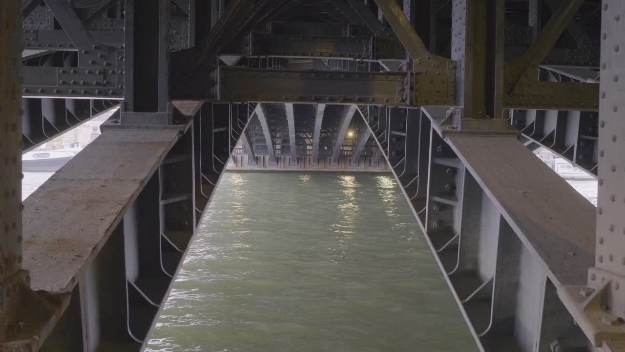 Under a bridge in Paris, the water reflects the steel structure of the bridge
