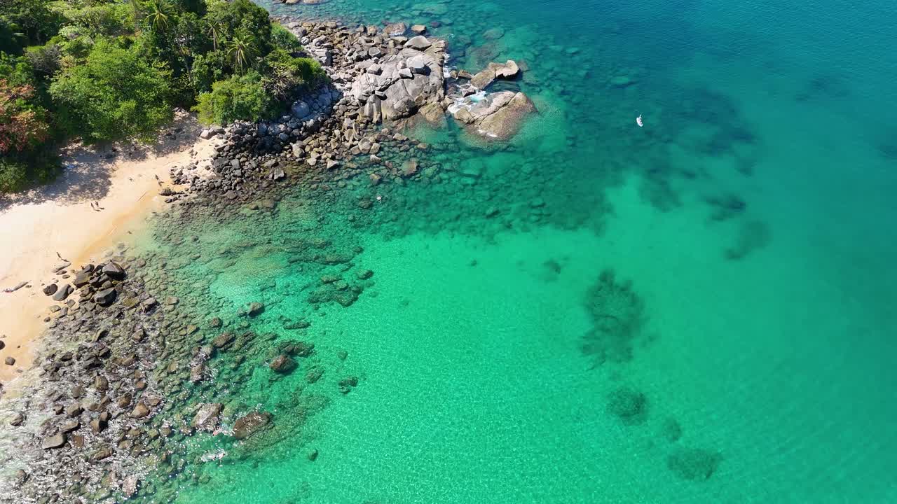 Aerial footage captures a serene beach in Phuket, Thailand, with turquoise waters and lush greenery under bright daylight