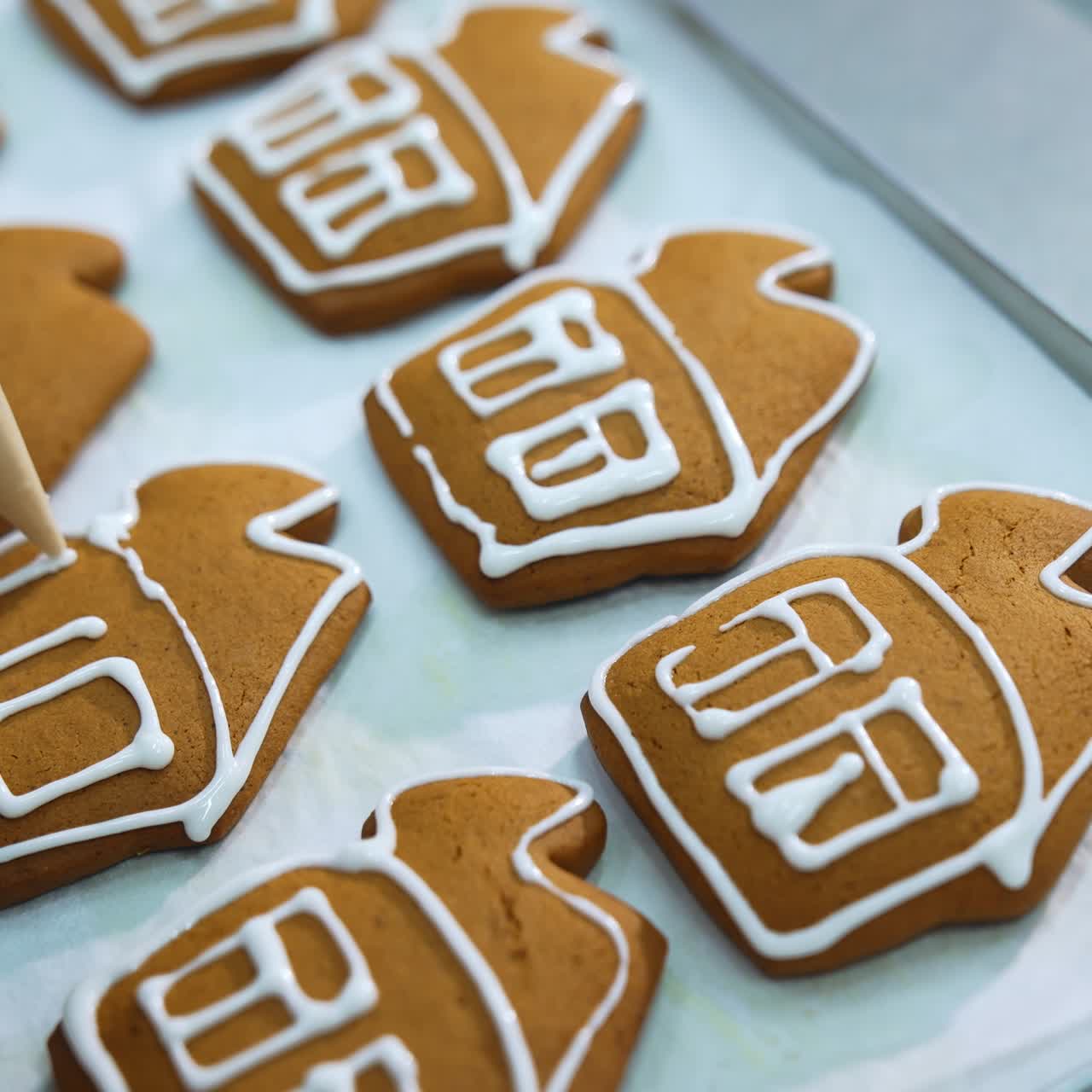 Primo piano di mani che decorano casette di pan di zenzero con glassa bianca. Produzione di pasticceria in una fabbrica di dolciumi
