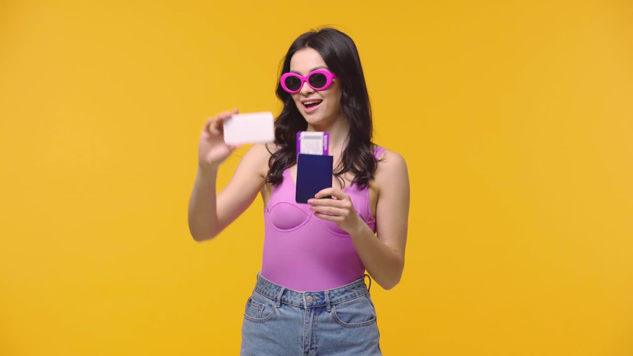 mujer tomando una selfie con pasaporte y billete de avión aislado en amarillo