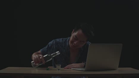 hombre asiático animando y bebiendo vodka durante una llamada de video en una computadora portátil con fondo negro