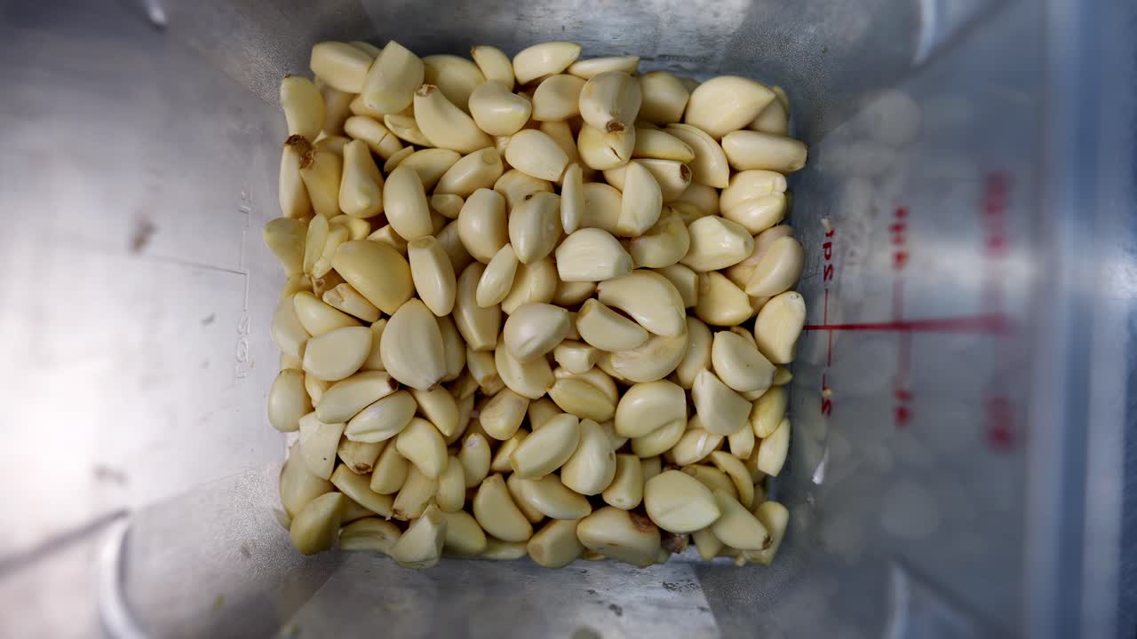 Slow motion and close up view of Garlic cloves falling into a measuring cup.