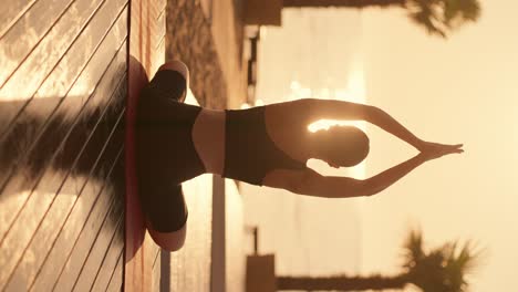 Vertical-video:-a-brunette-in-a-black-sports-uniform-meditates-and-puts-her-hands-in-a-namaste-position-on-a-sunny-beach-in-the