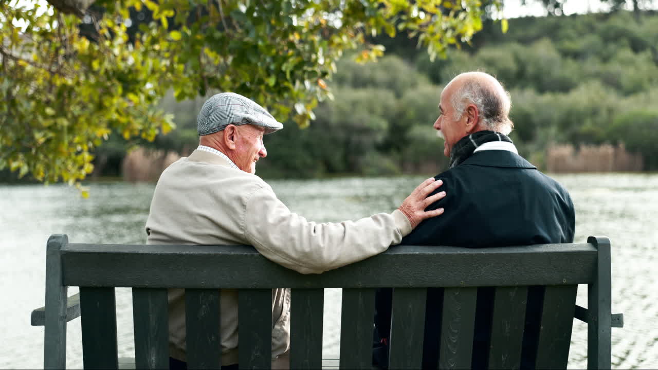 Two elderly men sitting on a bench by a lake