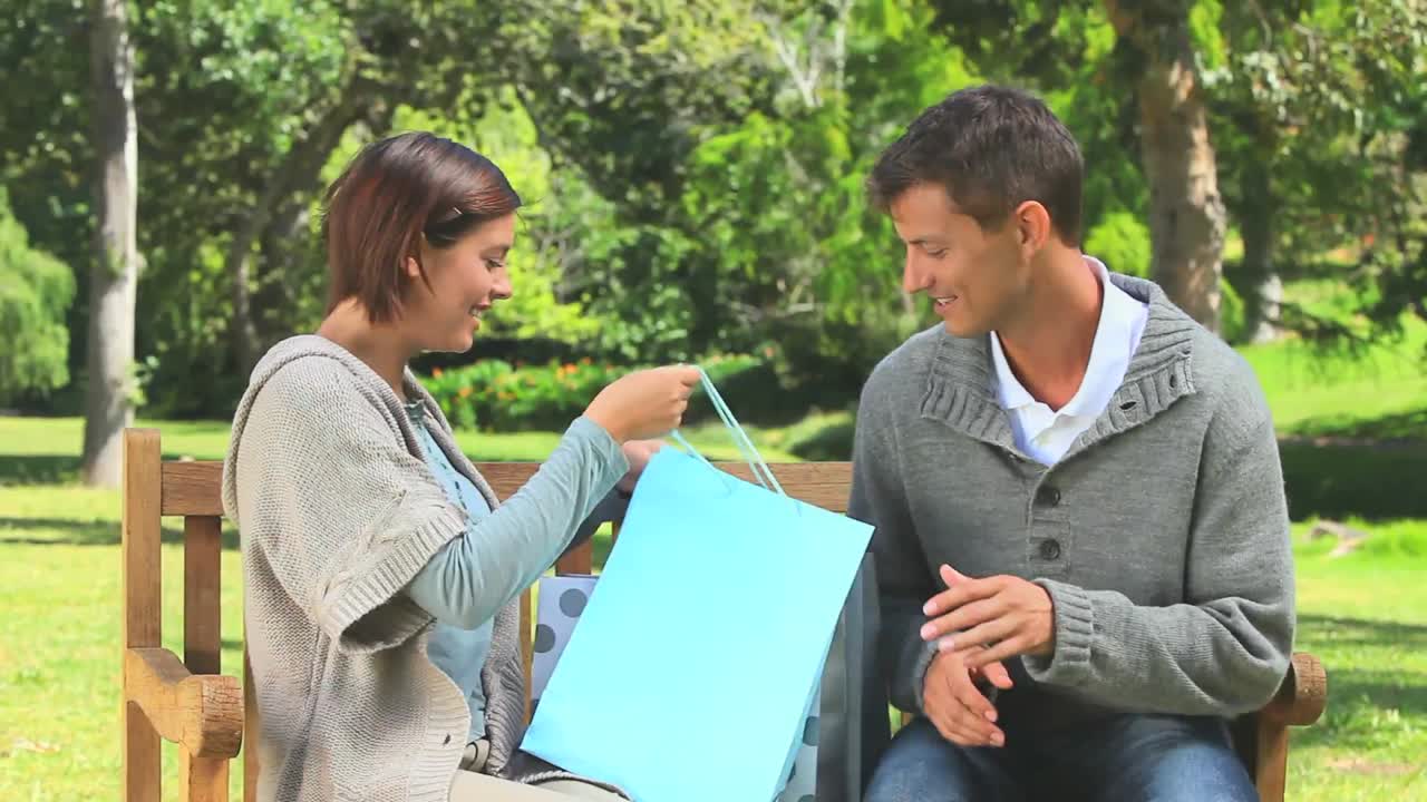 una joven pareja sentada en un banco con sus compras