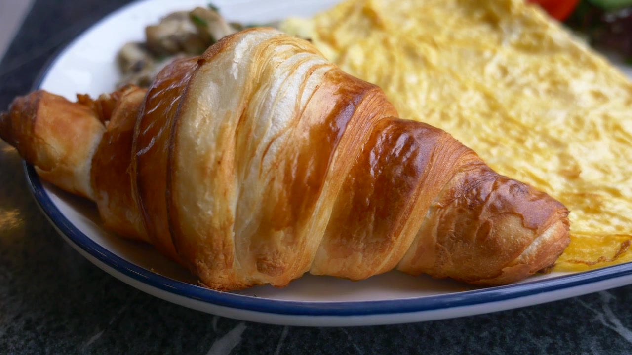 Croissant fresco e dorato servito con omelette su un piatto