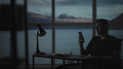 silhouette of a man sitting at a table looking at a mobile phone thinking and analyzing the stock market solving personal problems repayment of loans internet banking