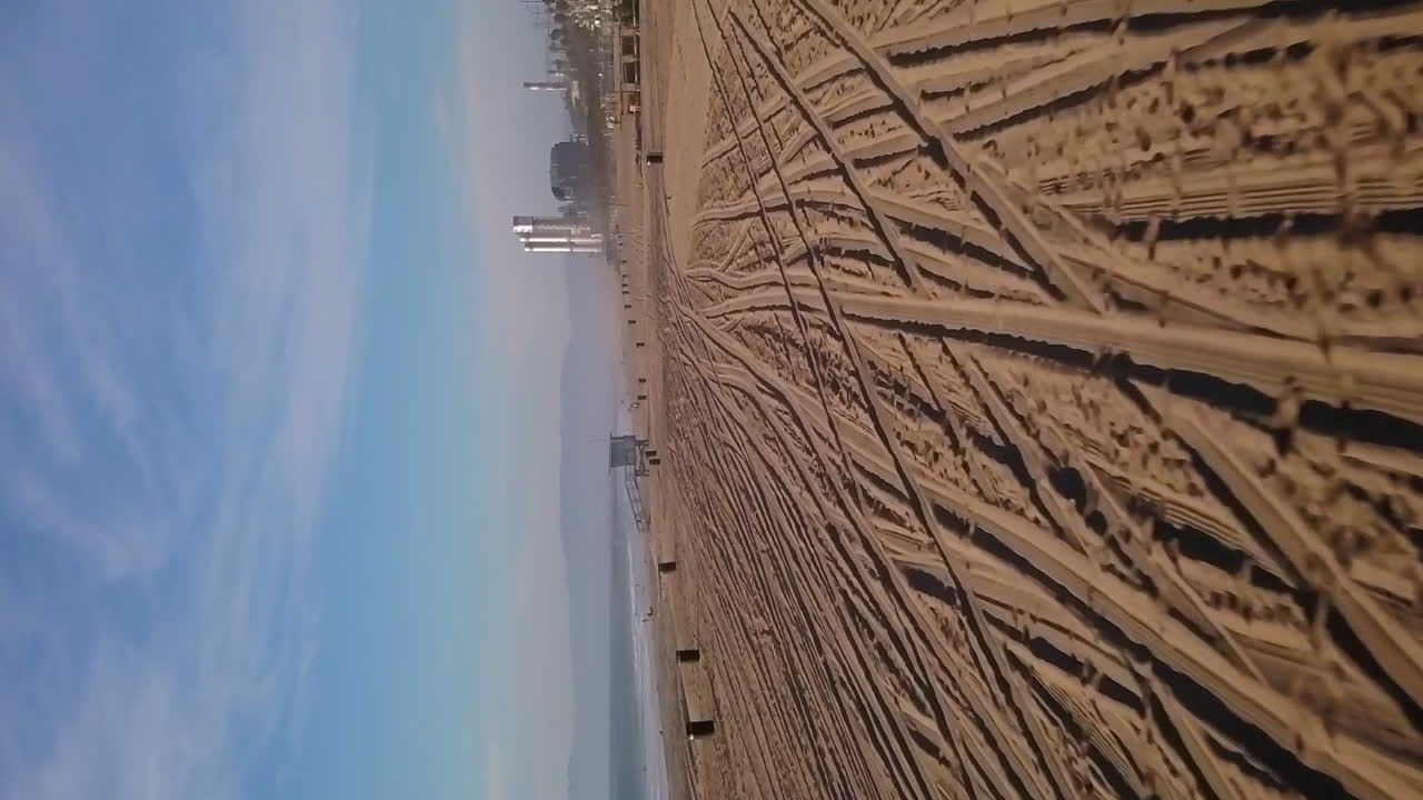 huellas de neumáticos en la arena de la playa de manhattan en los ángeles, california - orientación vertical aérea