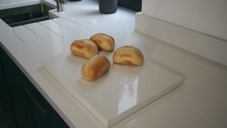 modelo femenino poniendo panecillos calientes en una encimera de cuarzo en una cocina moderna