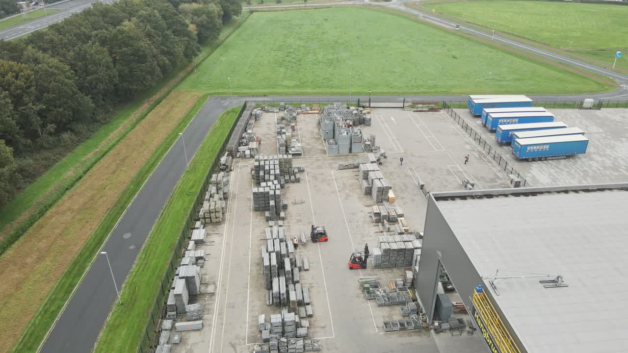 Aerial of a large industrial storage yard with forklift trucks moving construction materials