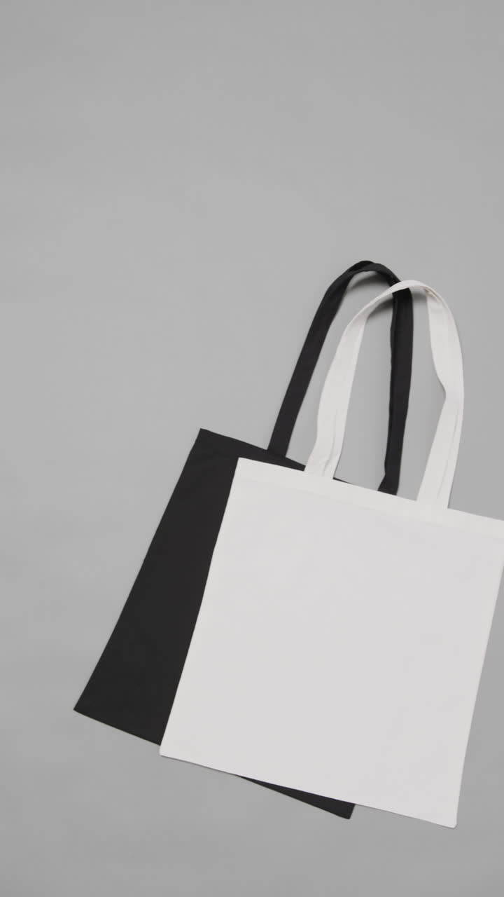 Vertical video of white and black bags on white background, copy space, slow motion