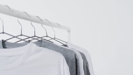 video of white and grey t shirts on hangers and copy space on white background