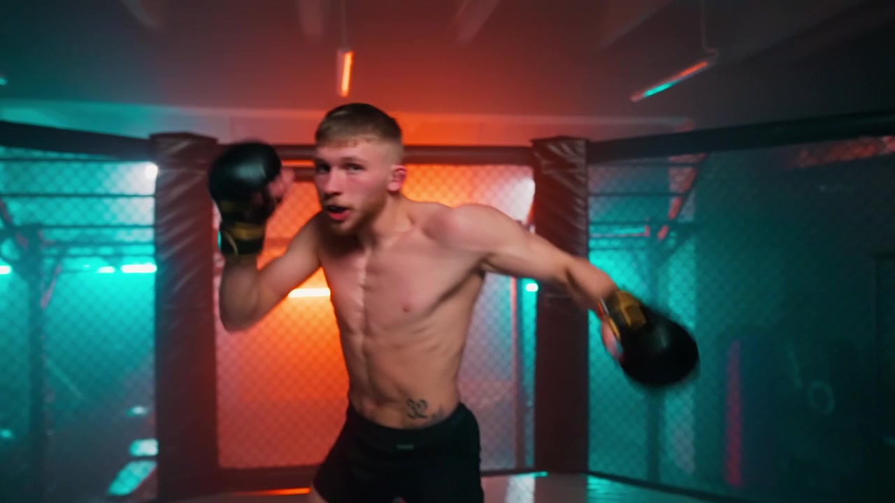 Young Male Boxer Training in a Neon Lit MMA Cage