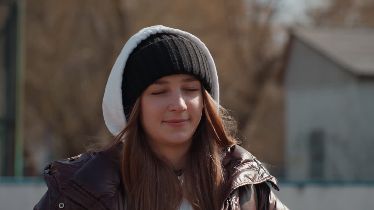 커뮤니티 골대 옆에서 편안한 자세로 후드티를 입고 캐주얼 재킷을 걸친 채 긴 머리를 하고 부드러운 햇살을 받으며, 애니메이션 같은 표정으로 이야기를 나누는 백인 십 대, 친근하고 대화적인 분위기