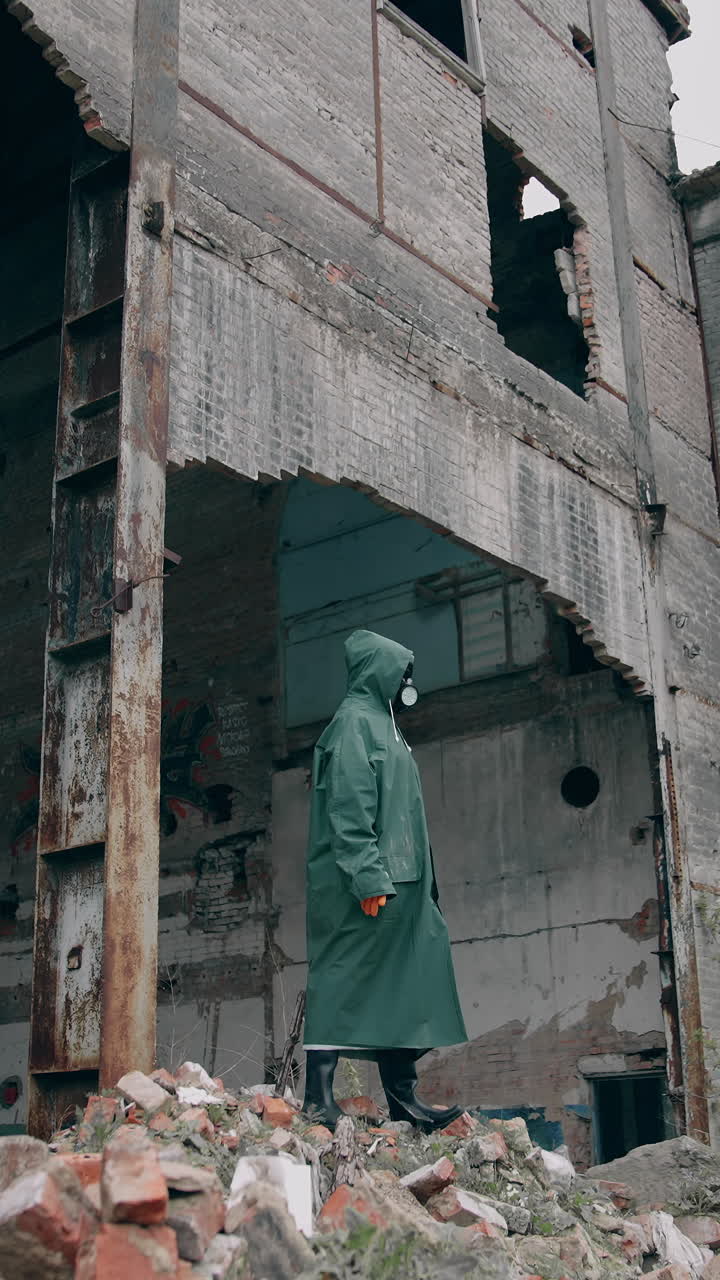 Survivor in safety suit in ruined place. Man in gas mask and protective wearing standing alone in abandoned place. Post-apocalyptic concept. Vertical video