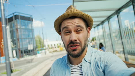 close-up view of caucasian young happy man traveller talking, waving hands and smiling at the camera outdoors in summer