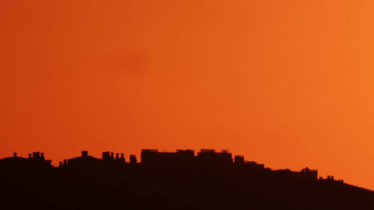 Silueta de un horizonte urbano contra un cielo de atardecer naranja intenso