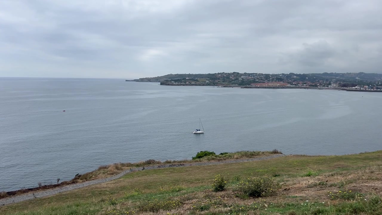 Vista elevada da costa do Golfo da Biscaia com um veleiro e a cidade de Gijón ao fundo