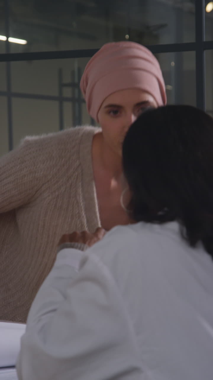 Vertical Video Of Serious Young Woman Patient Wearing Headscarf Undergoing Chemotherapy Treatment For Breast Cancer Meeting With Oncologist Or Doctor In Hospital 1
